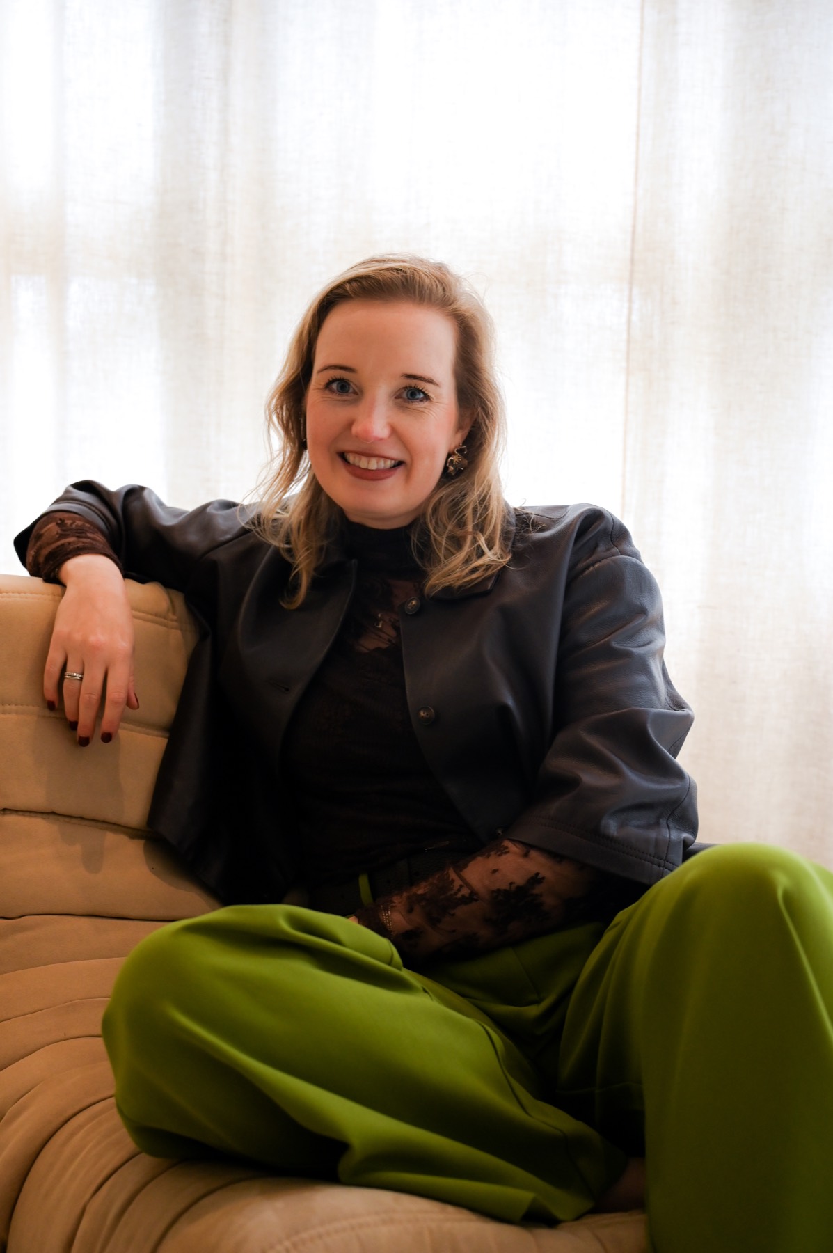Selma zit op een bank in een groene blouse en lacht naar de camera