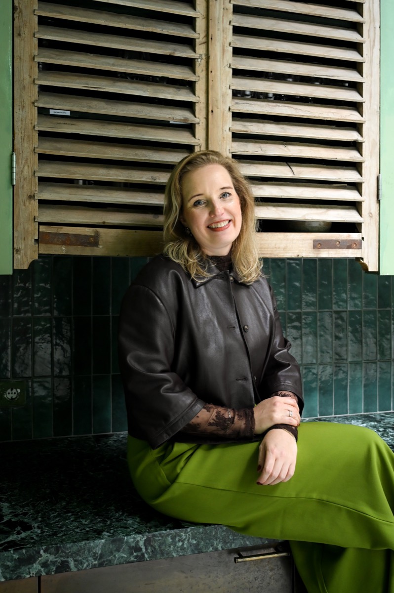 Selma zit op een groen marmeren keukenblad voor een wand van donkergroene tegels.
