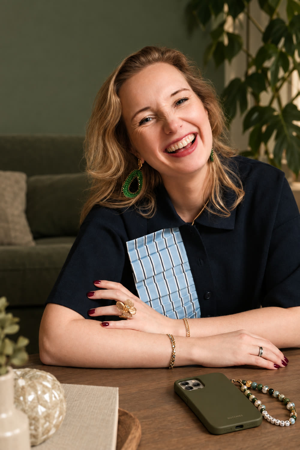 Selma van Studio LEEF Interieur lachend aan tafel in een woonkamer met een groene wand